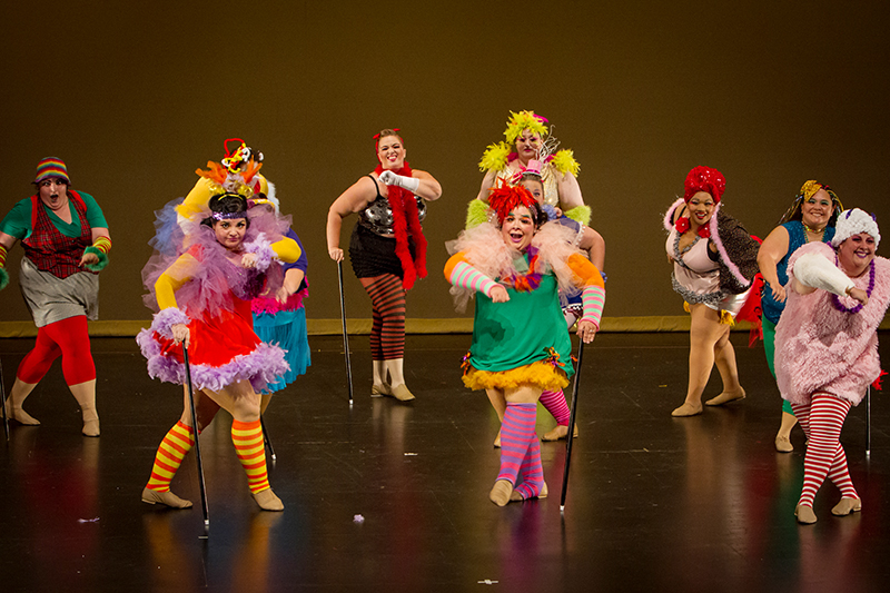 Ten dancers face front onstage in various colorful costumes.