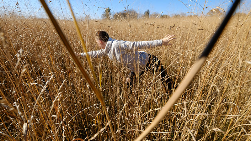 Emily leans forward in a field, one arm extended in front and one behind.