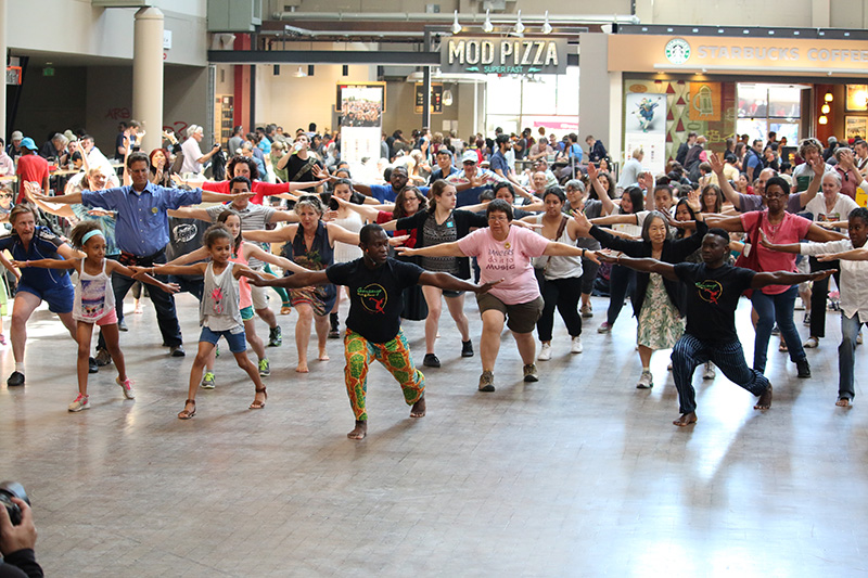 Etienne teaches a workshop to a large group of people in a mall. 