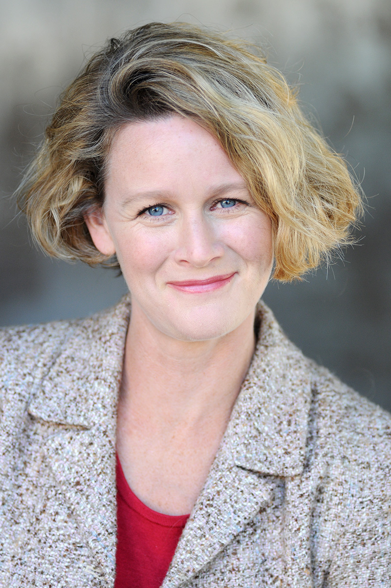 A headshot of Erin wearing a blazer and smiling.