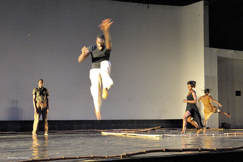 Four dancers are onstage. The dancer in the four ground is jumping with their legs tucked under them.