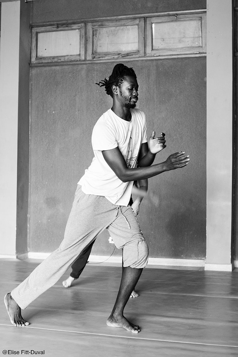 Momar takes a lunge with his arms crossed in front of him. The photo is in black and white.