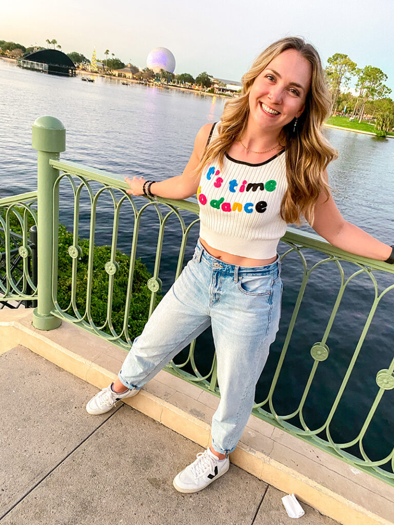 Alex standing and smiling at a riverfront with a shirt that says, "It's time to dance."