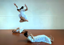 Two dancers dressed as patients lay on the floor while a third dancer dressed as a nurse leaps above them.