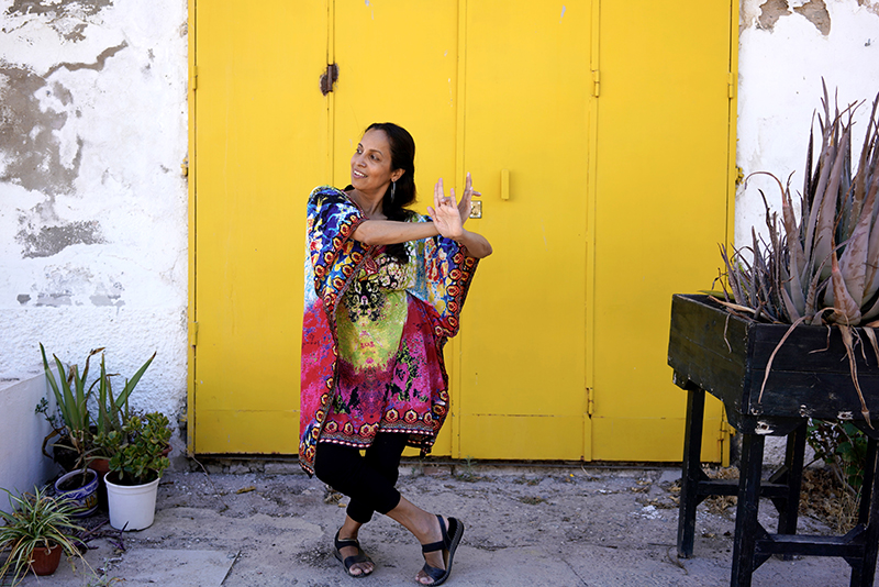 A woman doing an Indian classical dance step in front of a yellow door.