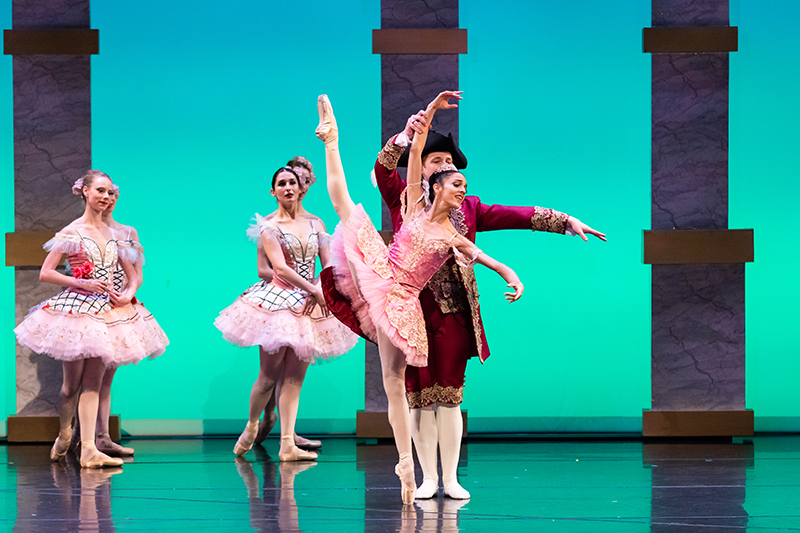 Michelle being partnered in ecarte derriere on pointe, wearing a pink tutu against a green lit stage.