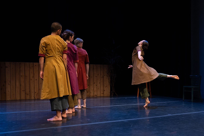 A line of dancers onstage look back at a soloist doing an arabesque