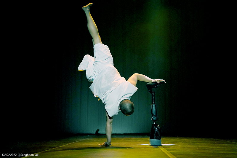 A dancer does a handstand onstage with one hand on the ground and another on his prosthetic.