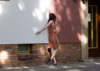 Shannon leans on a building with her hand on a white wall and her body and head turned away on a pick wall.