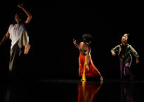 Three Black dancers make shapes against a black backdrop onstage.