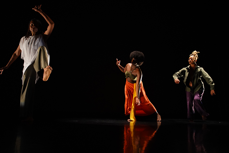 Three dancers make shapes against a black backdrop onstage.