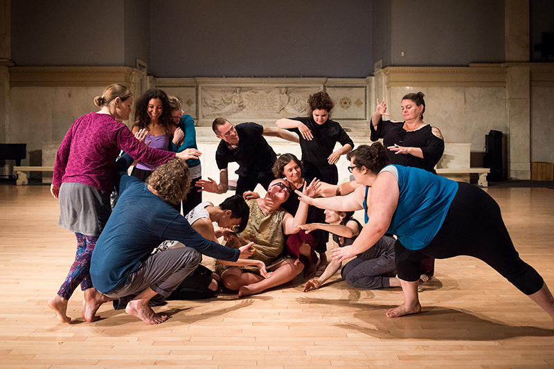 A group of people make shapes together with their bodies in a dance studio.