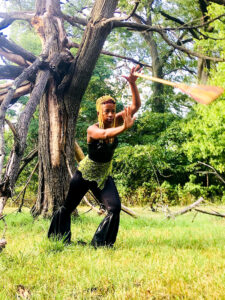Photo of Donne Lewis dancing with broom in forest