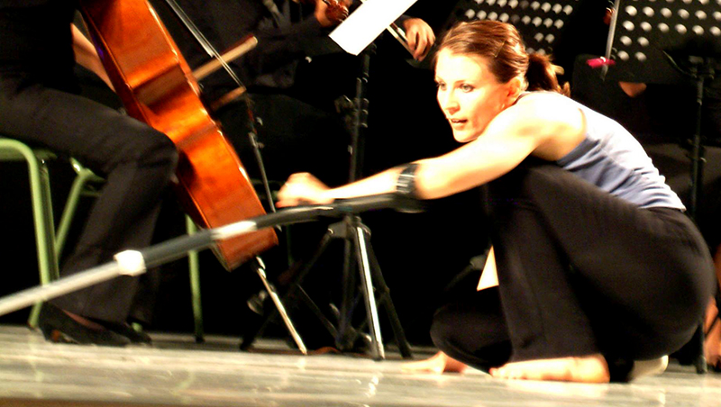 Nadia crouched low with her crutch in front of a cello