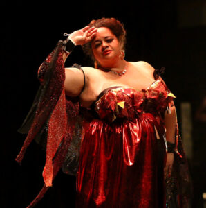 Tigress stands wearing a red dress, one arm brought up to her brow.