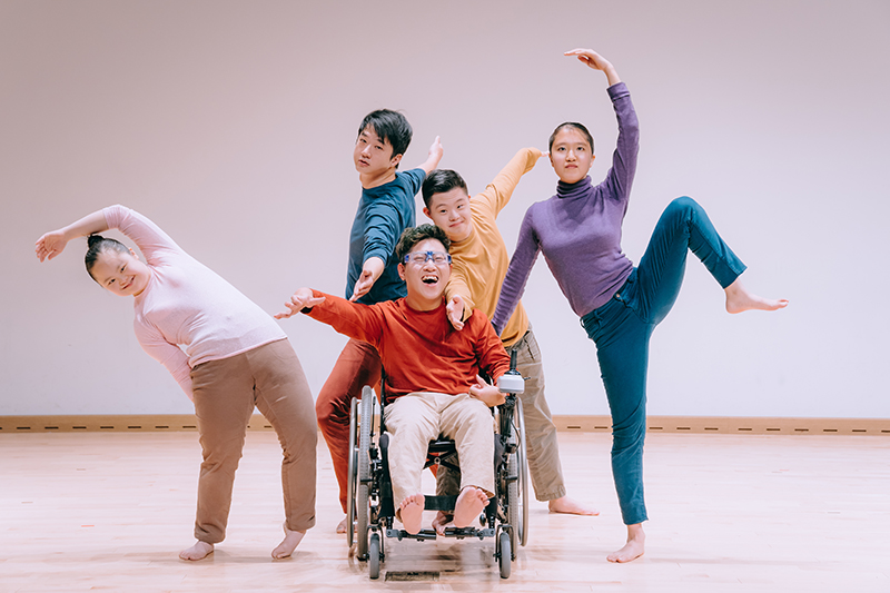 Five dancers with various disabilities make shapes. They are wearing bright colors.