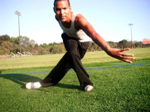Daniel dances on grass in a field. He bends low with his arm to the side.