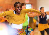 Rujeko smiling with her arms to the sides teaching a class with students behind her.