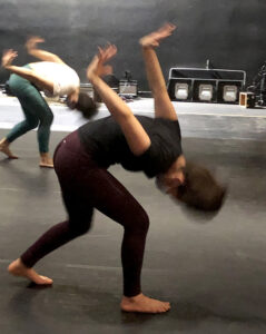 Two students bend over with their hands raised behind them with flexed wrists.