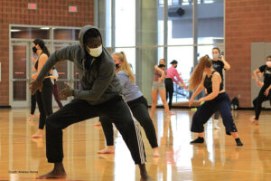 Momar is in a wide stance with arms to one side. Students follow behind him.