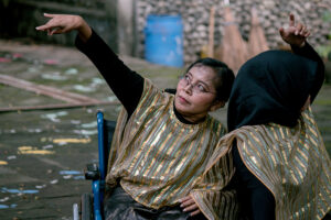 Lusi reaches upward as another dancer in a wheelchair leans into her.