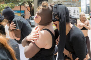Isabel leans back into another dancer, both wearing cloth masks over their faces.