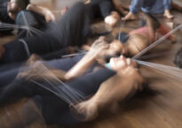 Several blurry dancers writhe on the floor with what appear to be strings connecting them.