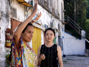 One woman lifts her arms overhead as another woman looks on.