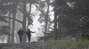Two figures dancing side by side in a rainy forest.