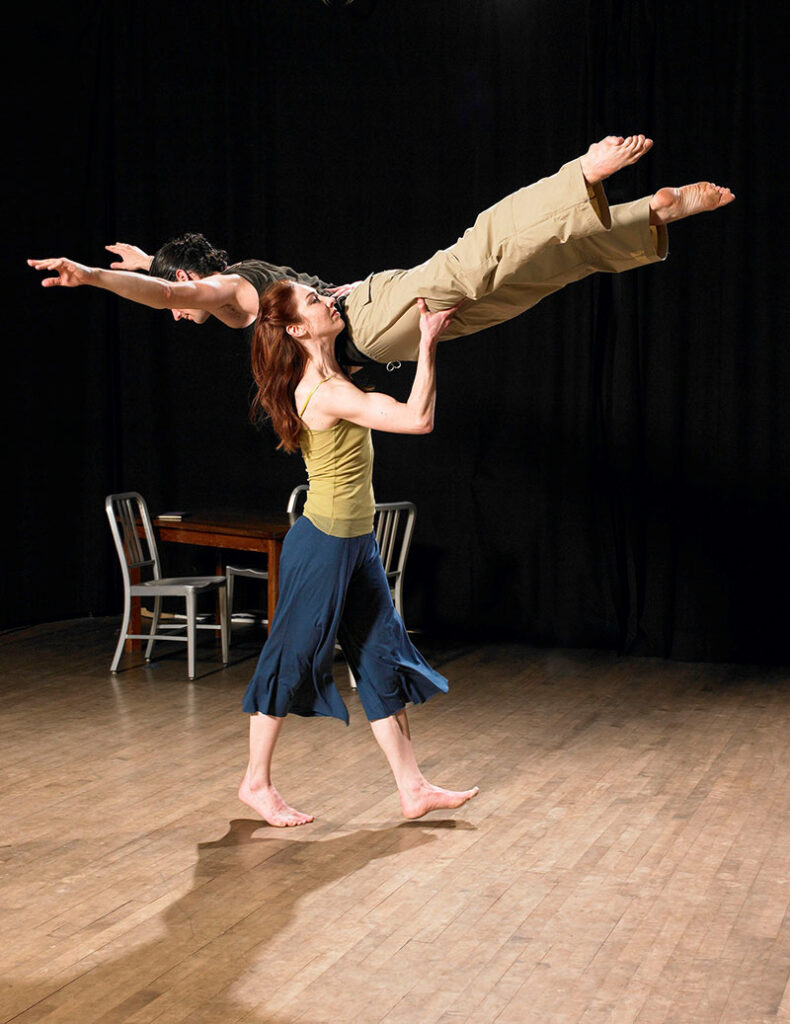 One dancer onstage lifts another in a plank-like position
