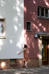 Shannon leans on a building with her hand on a white wall and her body and head turned away on a pick wall.