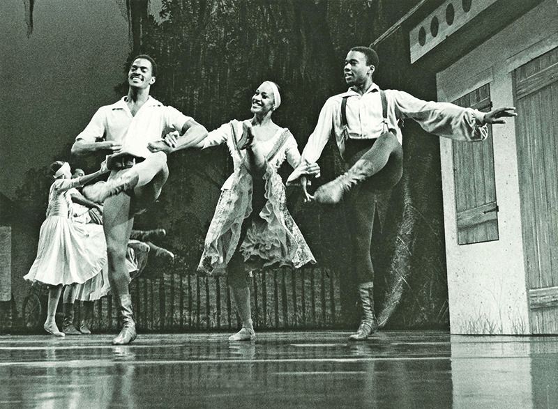 Two men accompany a woman in a ballet. The photo is in black and white.