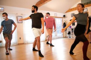 Bianca leads a group of men in a gentle stretch in a studio.