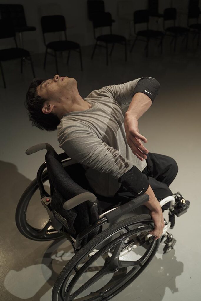 Wonyoung is photographed above his wheelchair. He is sitting in his chair at an angle and leaning back with his arm crooked into his chest.
