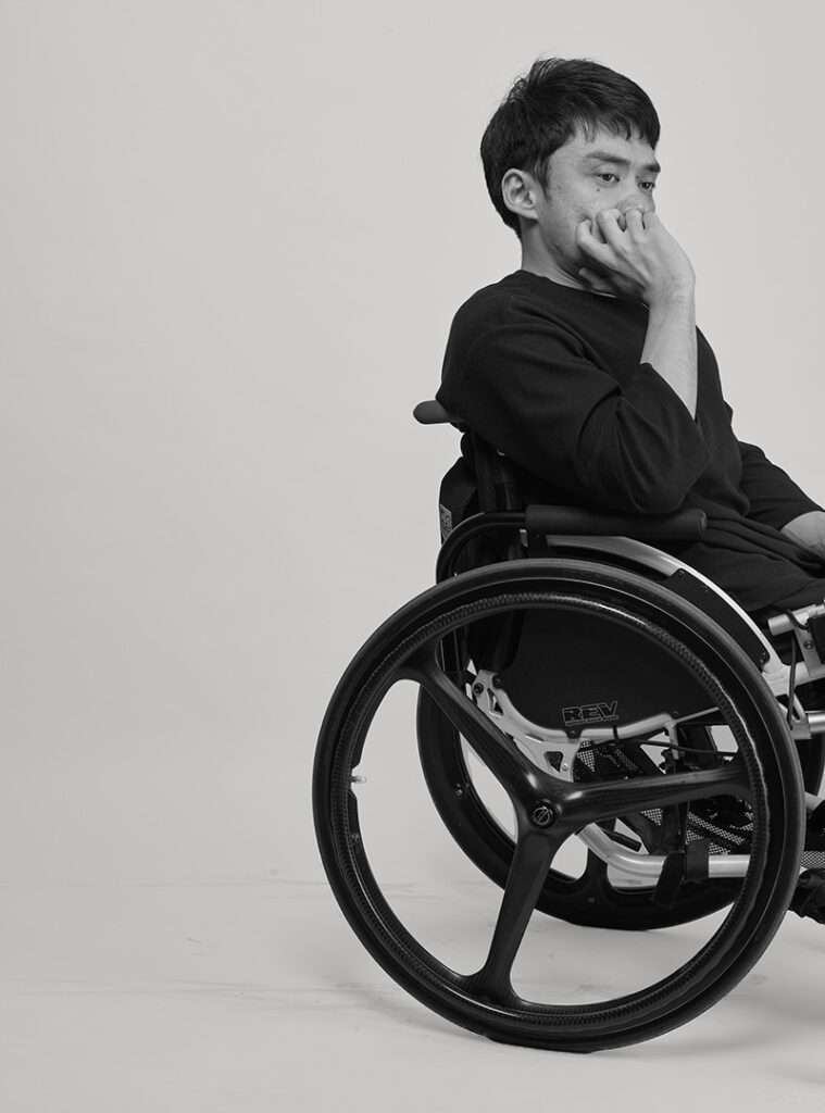 A black and white photo of Wonyoung sitting in a wheelchair with his chin in his palm.
