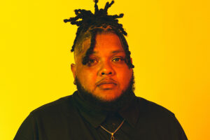 A headshot of P-top wearing a black shirt against a yellow background.