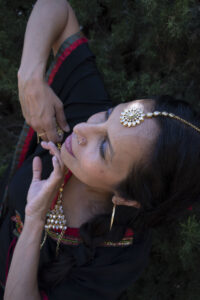 The camera is above Shebana's head. She has Indian jewelry on her head, neck and earrings. Her hands are close to her chest.