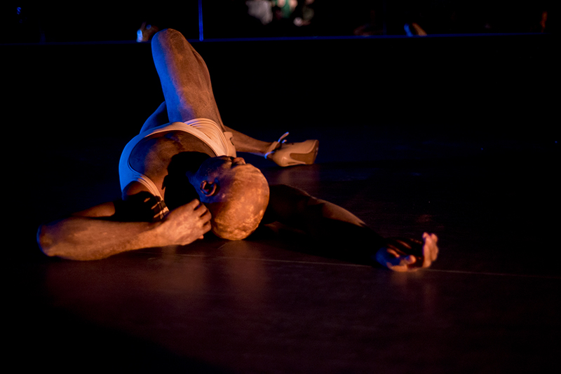 Darrell lays on the stage with one arm above his head and one leg bent at the knee.