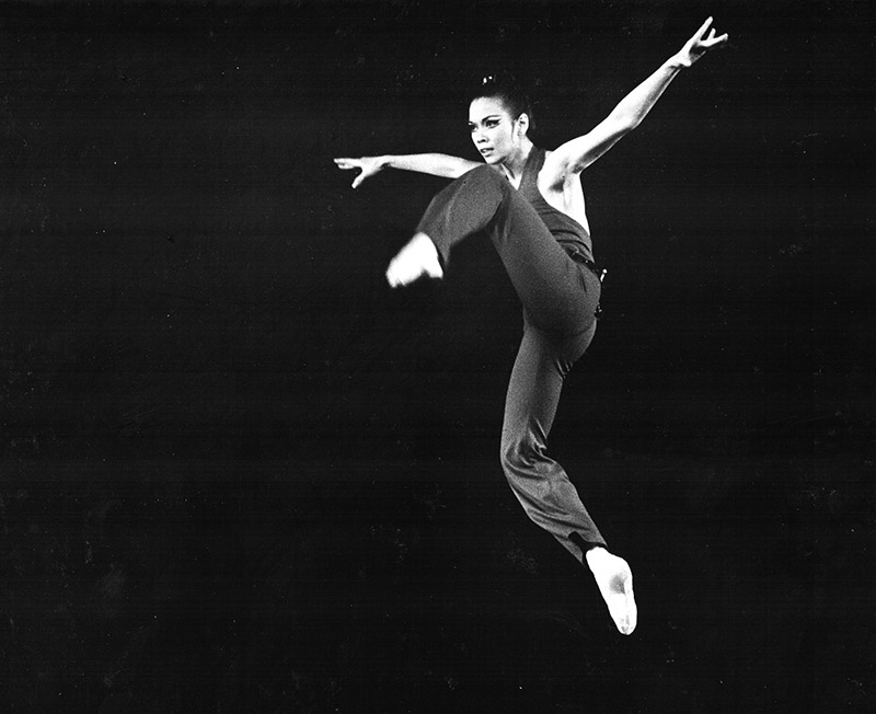 An old photo of a ballet dancer onstage in a double attitude leap.