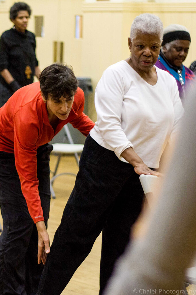 Naomi helps an older dancer extend her leg behind her.