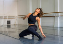 A dancer in a studio is low on her knee and foot, looking upward.