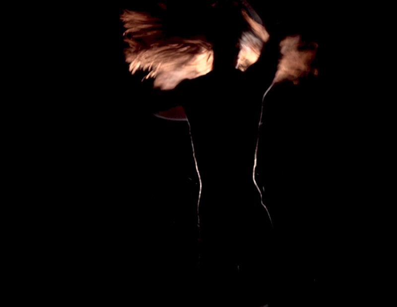 A backlit blurry image of a dancer with her hair moving with her as she twirls.