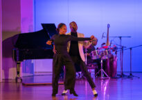 Sekou McMiller partners Desiree Godsell onstage in front of a piano.