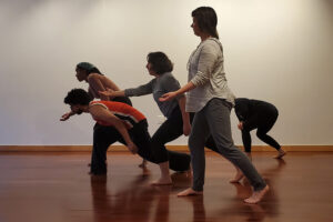 Five performers face the side and reach forward. They are at various levels.