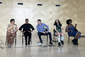 Five people sit in a row on chairs smiling and laughing.