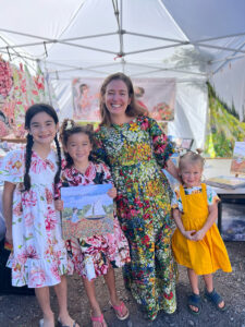 Julia stands with three little girls outside, all wearing bright floral printed dresses.