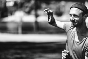 A black and white image of Alessandro outside wearing a beanie and lifting one arm. He is to the right of the frame.
