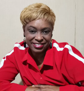 A headshot of Gladys smiling with arms crossed in front of her. She is wearing red.