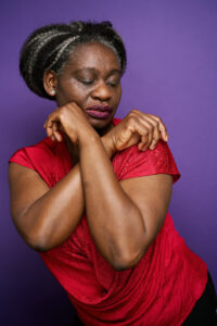 'Funmi is pictured from the waist up in a red shirt with her arms crossed and looking slightly downward.