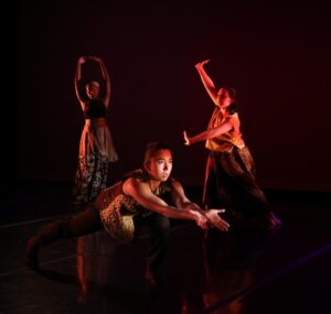 Three dancers onstage in low red lighting make three different poses.